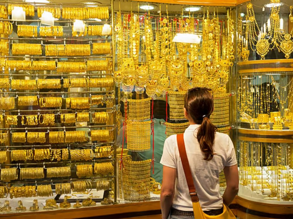 Woman standing outside a jewellery shop in Dubai showcasing UAE gold jewellery offers despite high gold prices.